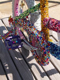 a colorful bicycle with beads on the handlebars is parked on a wooden bench