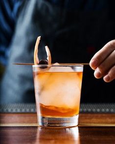 a person holding an orange peel in front of a glass filled with ice and liquid