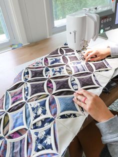 a woman is using a sewing machine to sew on a quilted table top