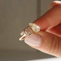 a woman's hand holding an engagement ring with two pear shaped diamonds