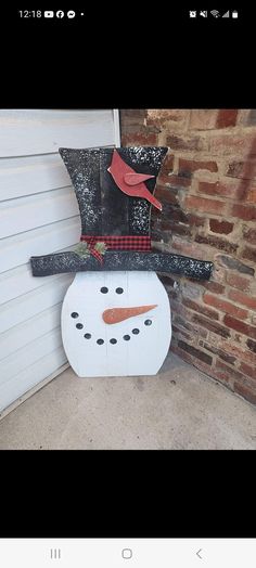 a snowman with a red bird on it's head and hat sitting in front of a garage door