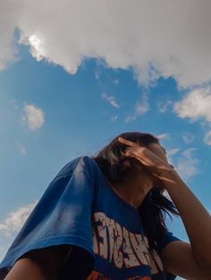 a woman standing under a cloudy blue sky with her hands to her face and one hand on her head