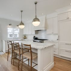 a large kitchen with white cabinets and marble counter tops, along with wooden flooring