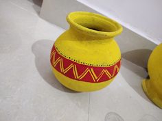 a yellow and red vase sitting on top of a white floor next to another yellow vase