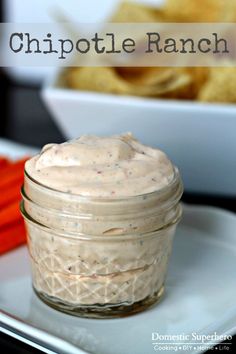 a small glass jar filled with food on top of a plate next to some chips