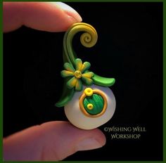 a hand holding a green and yellow brooch with flowers on it's back