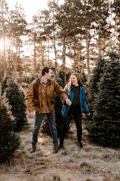 an engaged couple holding hands and walking through christmas trees