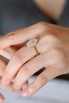 a woman's hand holding an engagement ring with a pear shaped diamond on it