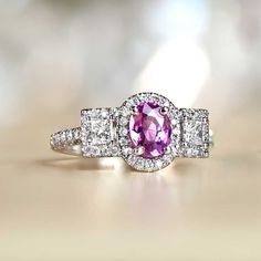 This 18k white gold three stone ring features a 1.01 carat pink sapphire, flanked by two princess cut diamonds with a combined weight of 0.69 carats. All three stones are set in prongs and surrounded by halos of round brilliant cut diamonds. Additional round brilliants are set in prongs along the shoulders and down the shank. The additional diamond weight on this ring  is approximately 0.84 carats.
The measurements of this ring including the side stones is approximately 15.95mm x 9.85mm.
This ri Luxury Pink Cubic Zirconia Wedding Jewelry, Gia Certified Pink Sapphire Ring In Platinum, Elegant Three Stone Pink Sapphire Jewelry, Elegant Pink Three Stone Rings, Pink Sapphire Three-stone Jewelry, Pink Three-stone Sapphire Jewelry, Pink Sapphire Three Stone Jewelry, Fine Jewelry Pink Three Stone Jewelry, Fine Pink Three Stone Jewelry