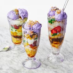 three desserts with ice cream, fruit and sprinkles in them on a marble table