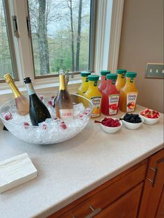 bottles of wine and fruit are on the counter in front of a window, along with other condiments