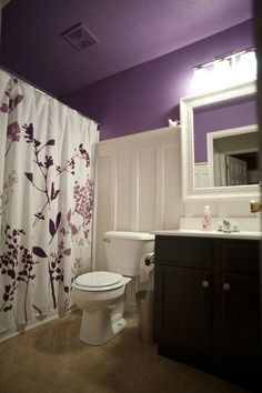 a bathroom with purple and white decor on the ceiling, shower curtain, toilet seat cover and sink