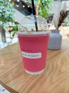 a pink drink sitting on top of a wooden table next to a cup with a straw in it