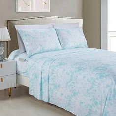 a bed with blue and white sheets in a bedroom next to a night stand on a wooden floor