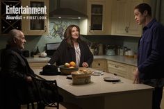 two men and a woman standing around a kitchen island