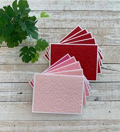 four cards with pink and red designs on them next to a potted green plant