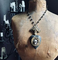 The Black Queen, Catherine de Medici, so named for her fascination with mysticism and the occult, is memorialized on back of this hand gilded ex voto.  The front showcases a skull within a decorative niche, and is strung on antique gold and jet glass rosary chain. The Ex Voto Sacred Heart was cast from an antique piece and recreated in plaster resin, then hand finished with acrylic paints, antiquing medium, and gilding paste to create a weathered black and tarnished gold finish. The back has an image of Queen Catherine de Medici salvaged from a vintage art book, then decoupaged with gold leaf, then varnished with antiquing medium to create a bit of tarnished appearance. Gothic Gold Engraved Jewelry, Gothic Hand-cast Halloween Necklaces, Gothic Bronze Engraved Jewelry, Gothic Engraved Bronze Jewelry, Collectible Gothic Brass Jewelry, Black Spiritual Jewelry With Antique Finish, Gold Gothic Engraved Necklace, Black Spiritual Collectible Jewelry, Vintage Black Skull Jewelry