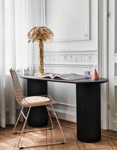 a table with a chair and a book on it in front of a window next to a palm tree