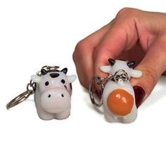 a hand holding two keychains that are shaped like cows