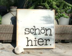 a wooden sign that says schon her next to some potted plants and a snail