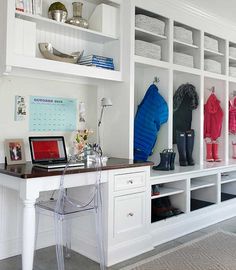 a white desk topped with a laptop computer next to a shelf filled with coats and boots