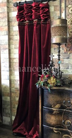 a red curtain is hanging in front of a brick wall and an ornate chest of drawers