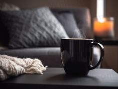 a black coffee cup sitting on top of a table next to a blanket and candle