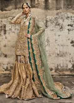 a woman in a gold and green outfit standing next to a wall with her hands on her head