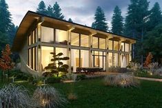 a modern house in the middle of a forest at night with its lights on and windows lit up