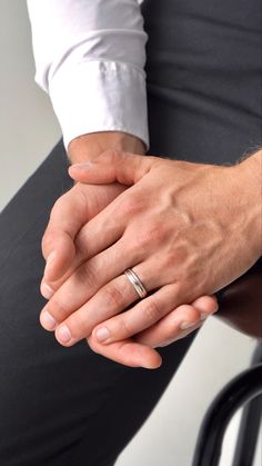 a man sitting on a chair holding the hand of another person wearing a wedding ring