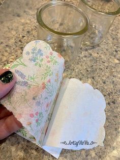 a person is holding an empty napkin near some jars on a counter top with flowers in them