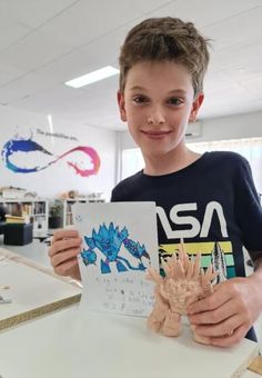 a young boy is holding up a paper with an image of a creature on it