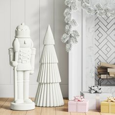 a white christmas tree next to a ceramic toy soldier and gift box on the floor