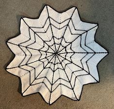 a white and black knitted spider web pattern on the floor in front of a gray wall