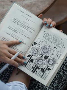 a woman is holding an open book with flowers on it and writing in the pages