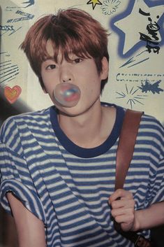 a young man blowing bubbles in his mouth while wearing a blue and white striped shirt