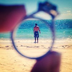 a man standing on top of a sandy beach under a magnifying glass next to the ocean