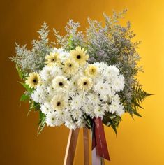 a bouquet of white and yellow flowers in a wooden vase on top of a table