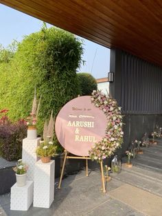 a pink sign sitting on top of a wooden floor next to flowers and potted plants