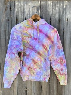 a colorful tie dye hoodie hanging on a wooden fence