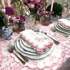 the table is set with pink and white plates, silverware, and vases