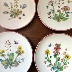 four plates with flowers painted on them sitting on a table