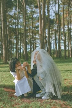 a bride and groom sitting on the ground in front of some trees with their hands together