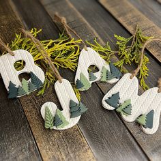 three ornaments are hanging on a wooden table with pine needles and twine around them