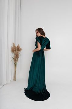 a woman in a long green dress standing next to a vase with flowers on it