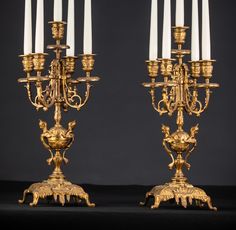 two golden candelabras with white candles on them