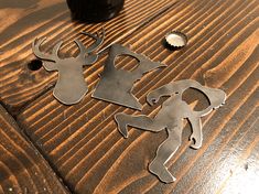 three metal deer cutouts sitting on top of a wooden table next to a bottle opener