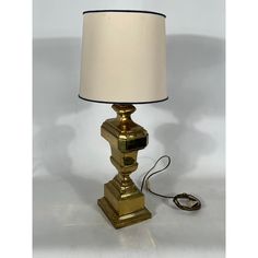 a gold lamp with a white shade on it and a cord attached to the base