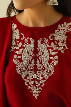 a woman wearing a red top with white embroidery on it