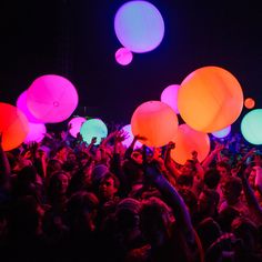 a large group of people at a concert with glowing balloons in the air above them